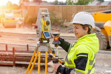 Close-up portrait of a woman site engineer surveyor working with theodolite total station EDM equipment on a building construction site outdoors