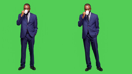 Male manager drinking cup of coffee on camera, serving caffeine beverage over full body green screen. Corporate worker enjoying hot refreshment drink, wearing business suit in studio.