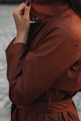 Fashion details of autumn long brown leather trench coat. Street style casual clothing. Woman walking alone in the city.
