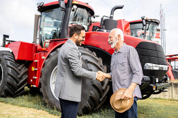 Farmer buying brand new tractor machine for agricultural business. Shaking hands with salesman for...