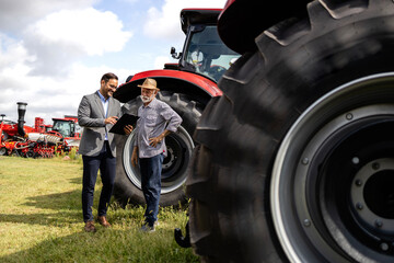 Tractor dealership and agricultural machines exhibition. Salesman and farmer discussing about the...