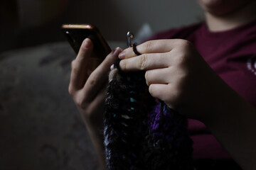 Skillful fingers of a young lady holding crochet hook and wool thread. Girls hands crocheting handmade jacket. Handcraft hobby, creating unique clothes for kraft art or farmer fashion market. - obrazy, fototapety, plakaty