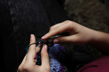 Skillful fingers of a young lady holding crochet hook and wool thread. Girls hands crocheting handmade jacket. Handcraft hobby, creating for kraft art or farmer fashion market. Selective focus - obrazy, fototapety, plakaty