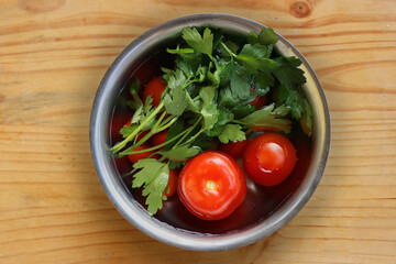 Fresh vegetables are being washed  in the metal bowl filled with cold water on the vintage cracked wooden cutting board. Organic tomatoes, parsley, celery. Top view. Copy space