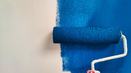 roller with blue paint on a white wall