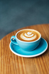 Top view of blue cup of tasty cappuccino with latte art on wooden table background.