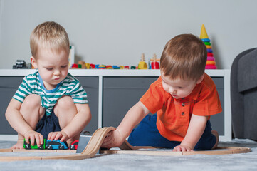 Two children boy play together with toys in interior of children's room..
