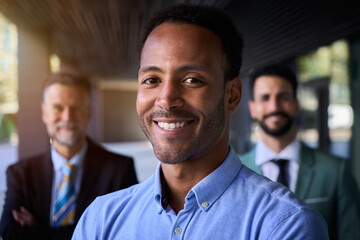 Smiling American black business man in suits looking happy at camera outside office building with...
