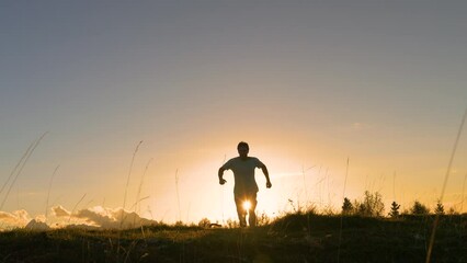LENS FLARE: Smiling man jumps with joy as he runs to top with his dog at sunset. He is happy and feels victorious when he reaches the picturesque alpine mountain top in golden autumn sunset light.