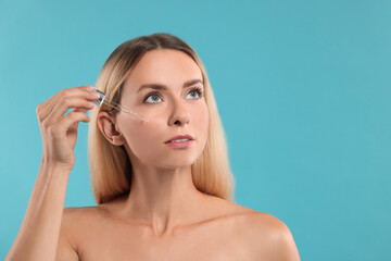 Naklejka premium Beautiful woman applying cosmetic serum onto her face on light blue background, space for text