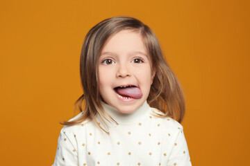 Funny little girl showing her tongue on orange background