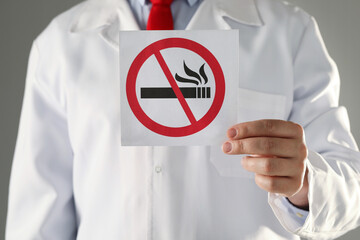 Doctor holding card with no smoking sign on gray background, closeup © New Africa