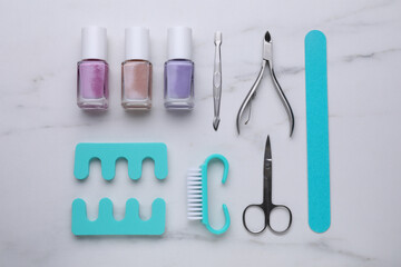 Set of pedicure tools on white marble table, flat lay