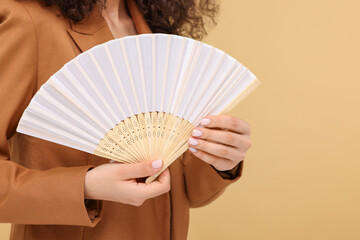 Woman holding hand fan on beige background, closeup. Space for text