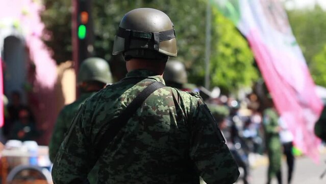 male soldier from the mexican army wearing the military uniform and helmet with the mexican flag waving in the background, during the parade of the mexican independence day celebration