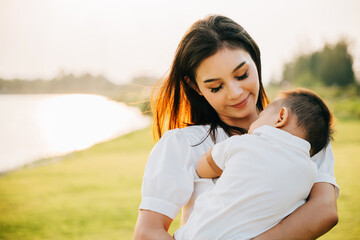 Obraz premium Portrait of a contented mother holding her sleeping son in a serene garden. Her face beams with joy and happiness as she takes in beauty of outdoors with her newborn. A moment of family care and bliss