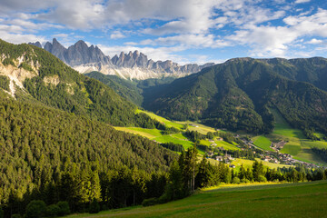 Picturesque landscapes of alpine highland valley of Val di Funes located at foot of rocky mountains of Italian Dolomites with green meadows, dense forests and charming rustic houses on sunny day