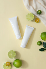 Over the beige background, two unbranded tubes are displayed with some fresh lime and kumquat...