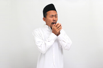 Unwell young Indonesian man wearing a songkok or peci or kopiah, is sneezing suffering from fever and flu, isolated on a white background