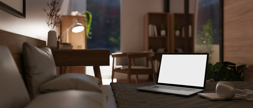 Close-up image of a white screen laptop mockup on bed in a modern and comfortable bedroom.