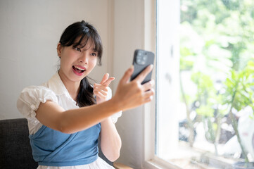 A pretty Asian woman is talking on a video call or recording a video on her phone in a coffee shop.