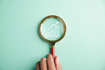 Trader attention to detail, Holding magnifier glass, hand inspects bar graph with rising arrow....
