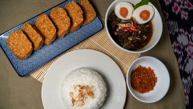 High resolution photo of Rawon, Indonesian black soup served with rice, salted egg, tempe goreng (fried tempe), and sambal (condiment)