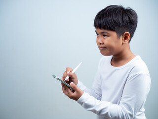 A boy in a white shirt is holding a white pen and smartphone on a white background. Shows thinking, pondering, and considering options.