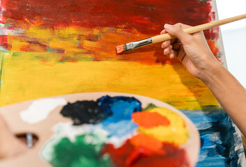 Close up hand Asian woman artist working on painting with brush and variant acrylic color. Female artist painter on canvas in creative studio as art concept