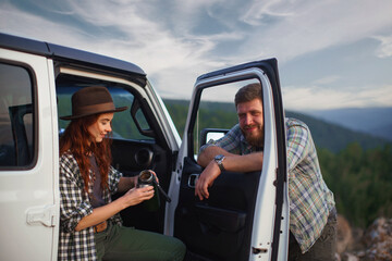 Naklejka premium Guy and girl travelers with off-road car drink tea from thermos.