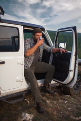 Portrait of hipster man traveler on background of car with tent on roof and mountains.