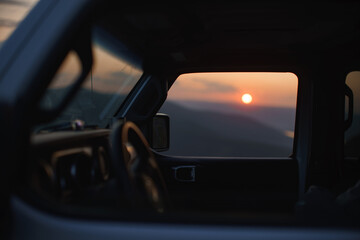 View of sunset in mountains through glass of off-road car.