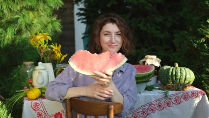 Beautiful woman eating watermelon while sitting at the table in her summer cottage on a sunny day