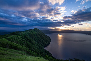 山間の湖の水面に太陽光が反射する朝。北海道の摩周湖。