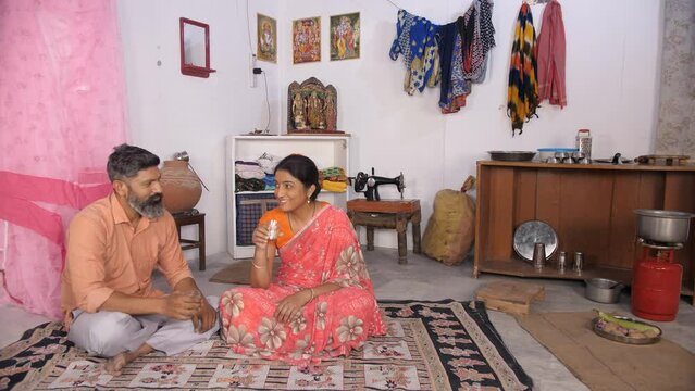 A lower middle class Indian couple chatting and having tea together - rural household  poor family. A middle-aged couple sitting on the floor - hardships in life  developing country  BPL card holde...