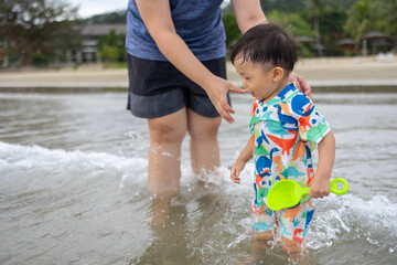 Happy 1-2 years old child enjoying playing on beach with splashing warm sea water