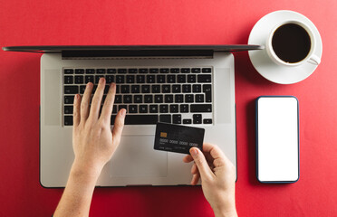 Caucasian woman with credit card using laptop and smartphone with copy space on red background