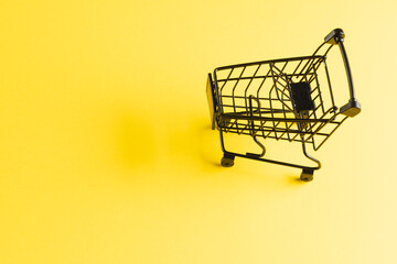 Black shopping trolley with copy space on yellow background