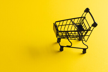 Black shopping trolley with copy space on yellow background