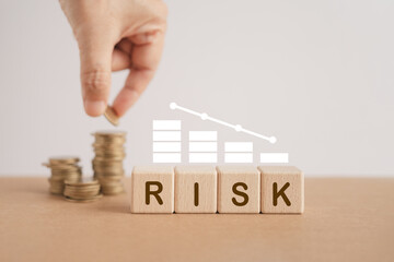 For financial risk assessment and  management concept. RISK word on wooden cube blocks and white bar graph with blurred hand arranged stack of coins