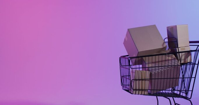 Video of boxes and shopping trolley with copy space over neon purple background