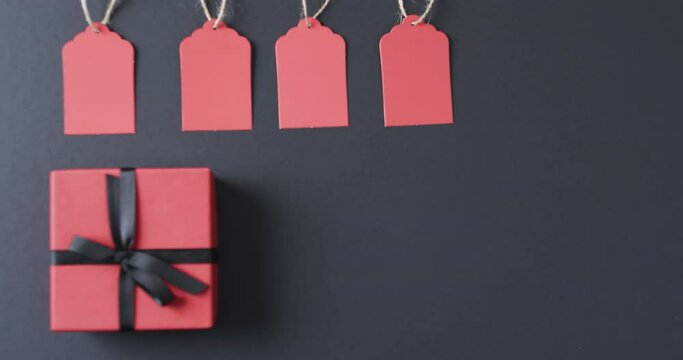 Video of gift tags on string, red gift box with ribbon and copy space on black background