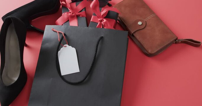 Video of gift bag, gift boxes with red ribbon, shoes, purse and copy space on red background