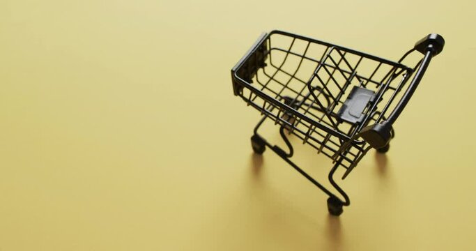 Video of empty shopping trolley with copy space on yellow background