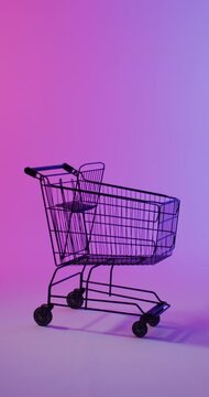Vertical video of shopping trolley with copy space over pink neon background