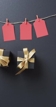 Vertical video of gift tags on string, gift boxes with ribbons and copy space on black background