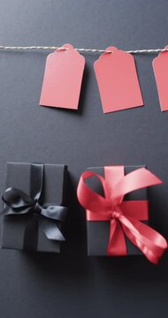 Vertical video of gift tags on string, gift boxes with ribbons and copy space on black background