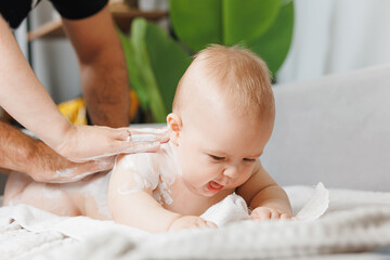Mother and father applying body cream on her little baby son at home
