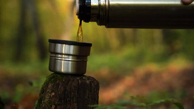 Pour hot tea from Temos into a cup in the autumn forest
