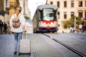 Woman traveler with suitcase and backpack walking on street. Travel and vacation in european city Olomouc, Czech Republic - obrazy, fototapety, plakaty